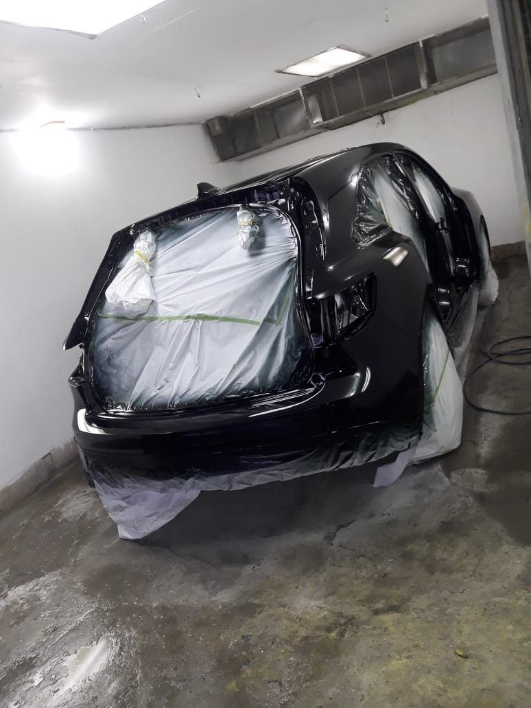 Black car body freshly painted, still masked, curing in the paint booth